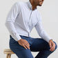A man sits on a stool in the Peter Millar Rommel Performance Twill Sport Shirt—a light checked shirt—paired with blue pants, in front of a plain background.
