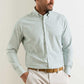 A man wears the Peter Millar Lewis Performance Twill Sport Shirt in light green and white check, featuring UPF 50+ fabric, paired with beige pants and a brown belt, against a plain background.