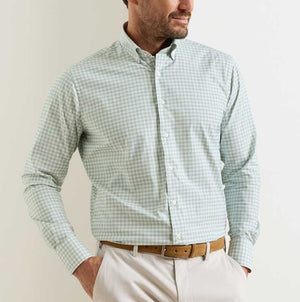 A man wears the Peter Millar Lewis Performance Twill Sport Shirt in light green and white check, featuring UPF 50+ fabric, paired with beige pants and a brown belt, against a plain background.