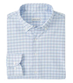 The Casey Performance Twill Sport Shirt by Peter Millar is a neatly folded long-sleeve button-down in light blue and white plaid, crafted from performance fabric. The label inside the collar reads "Peter Millar.