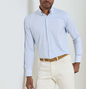 A man wearing the Peter Millar Casey Performance Twill Sport Shirt in light blue check, paired with beige pants and a tan belt, stands against a plain light-colored background.