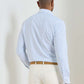 A man faces away, wearing the Peter Millar Casey Performance Twill Sport Shirt in light blue check, tucked into beige pants with a tan belt against a plain background. The performance fabric ensures comfort and durability all day.
