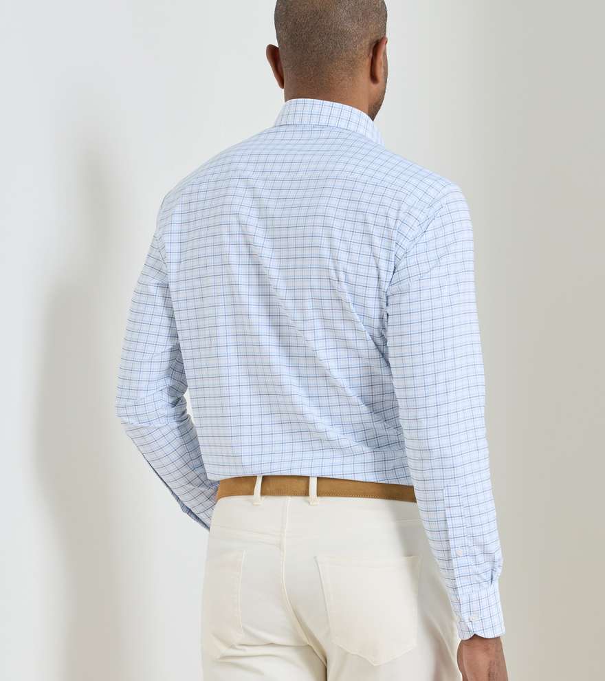 A man faces away, wearing the Peter Millar Casey Performance Twill Sport Shirt in light blue check, tucked into beige pants with a tan belt against a plain background. The performance fabric ensures comfort and durability all day.