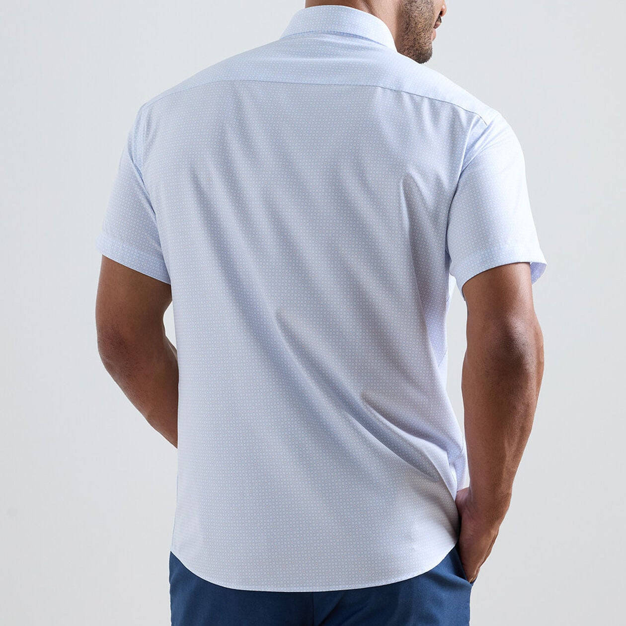 A man is shown from the back wearing the Peter Millar Baldwin Performance Sport Shirt in light blue UPF 50+ fabric with blue pants, set against a plain background.