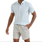 A man in a Peter Millar Whitehaven Sport Shirt, featherweight and light blue, paired with light gray shorts, stands with one hand in his pocket against a white background.