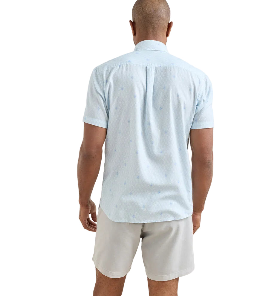 A man stands with his back to the camera, wearing a Peter Millar Whitehaven Sport Shirt in light blue and light-colored shorts against a plain white background.