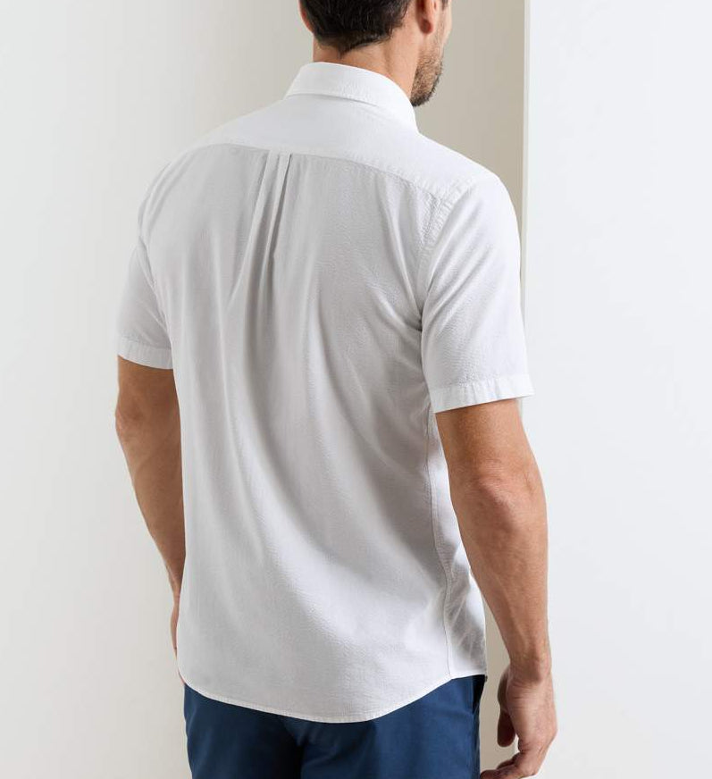 A man stands with his back to the camera, wearing the Peter Millar Seaward Cotton Lyocell Sport Shirt in white and blue pants, set against a plain white background.