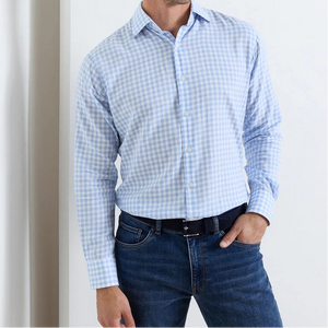 A man wearing a Peter Millar Breeze Cotton Lyocell Sport Shirt in light blue and white check, paired with dark blue jeans, stands against a plain background.