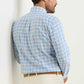 A man stands against a light wall, wearing the Peter Millar Waterrock Cotton Lyocell Sport Shirt in light blue and white plaid, paired with beige pants.