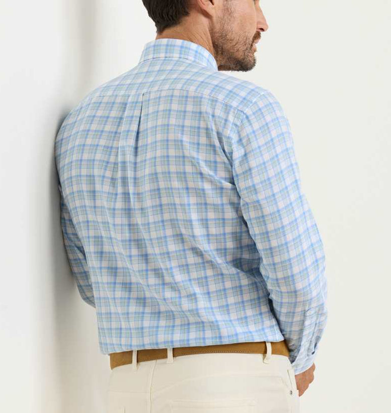 A man stands against a light wall, wearing the Peter Millar Waterrock Cotton Lyocell Sport Shirt in light blue and white plaid, paired with beige pants.