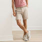 A person wears a red striped shirt, Peter Millar Bingham Performance Short, and white sneakers while standing indoors against a white wall with one leg crossed.