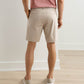 A person wearing Peter Millar Bingham Performance Shorts, a brown belt, red striped shirt, and light slip-on shoes stands facing away in a room with light-colored floors and walls.