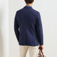 A man is seen from behind wearing the Peter Millar Bingham Performance Blazer in navy with beige pants, holding a brown-handled bag in his left hand against a plain background.