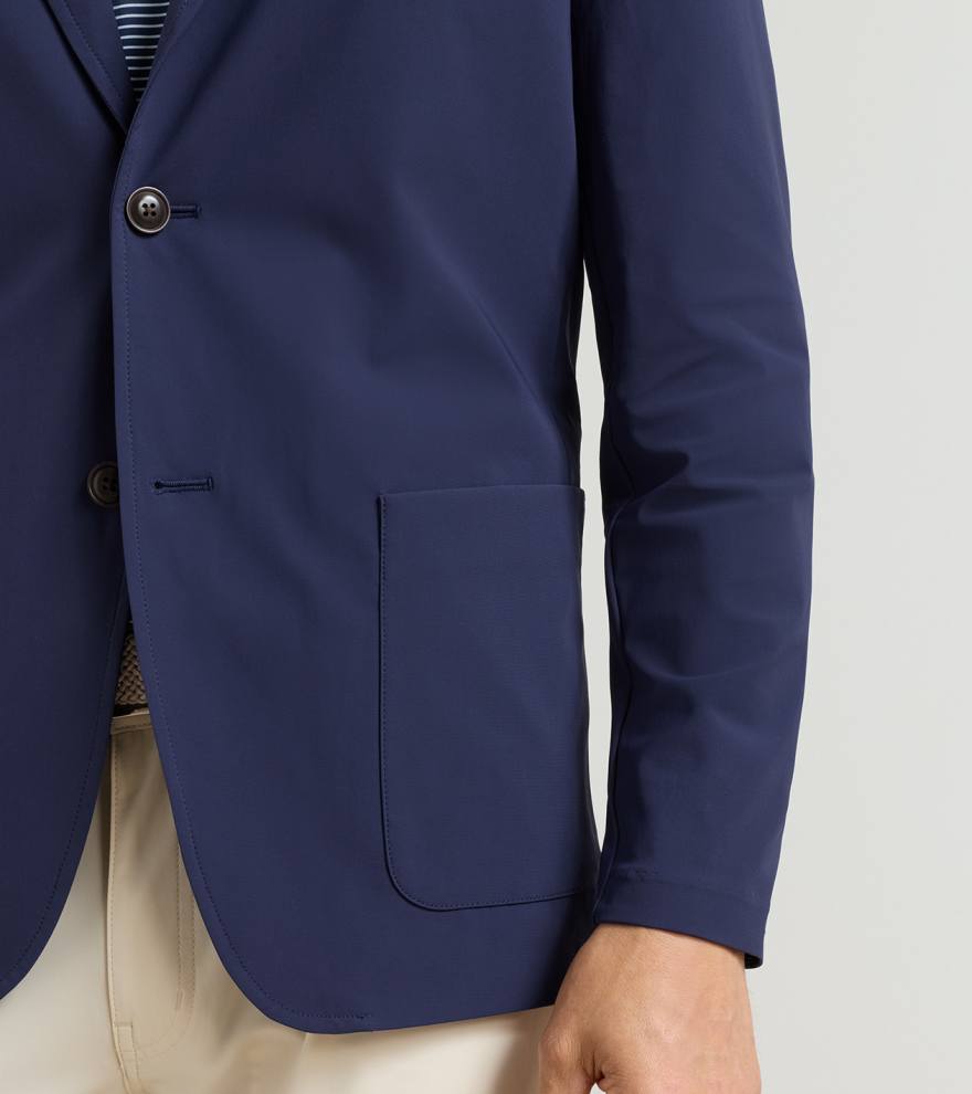 A person wearing the Peter Millar Bingham Performance Blazer in navy over a striped shirt and beige pants, with only their torso and right arm visible.
