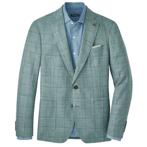 The Peter Millar Salisbury Windowpane Soft Jacket features a light green plaid with blue lines, crafted in lightweight wool. Shown with a blue button-down shirt and white pocket square on a white background.