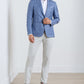 A man wearing the Peter Millar Reynolds Plaid Soft Jacket stands against a white wall and wooden floor, showcasing this light blue lightweight wool blazer as a versatile, casually refined wardrobe essential.