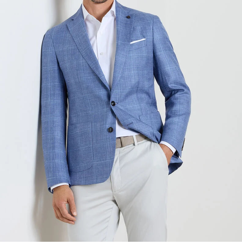 Man wearing the Peter Millar Reynolds Plaid Soft Jacket—a light blue checkered blazer—paired with a white shirt, light gray pants, and a belt. A versatile wardrobe essential showcasing European craftsmanship.