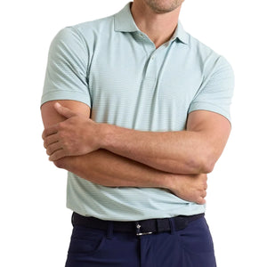 A man stands with arms crossed wearing a Peter Millar Ballad Performance Jersey Polo in light green stripes (UPF 50+) and dark blue pants.