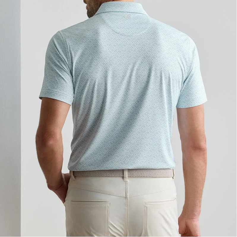 A man is seen from behind wearing a Peter Millar Wood Fired Performance Jersey Polo in light blue, featuring four-way stretch, tucked into beige pants with a textured belt.