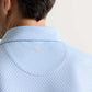 Close-up of the back of a man's neck and shoulders wearing the Peter Millar Mayfield Performance Jersey Polo in light blue pattern, featuring a small circular collar logo and offering UPF 50+ sun protection.