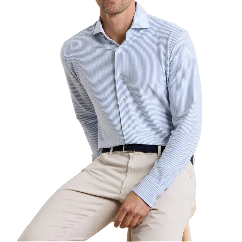 A man wearing the Peter Millar Excursionist Flex Stripe Sport Shirt and beige pants sits on a wooden stool against a white background.