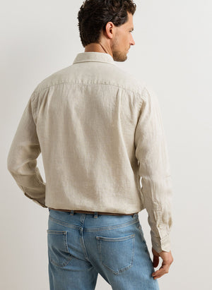 A man stands with his back to the camera, wearing the Peter Millar Astino Lino Sport Shirt—crafted from Italian linen with a cutaway collar and refined mother-of-pearl buttons—paired with blue jeans against a plain light-colored wall.
