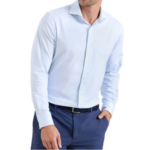 A man wears the Peter Millar Excursionist Flex Print Sport Shirt in light blue, tucked into navy blue pants, with one hand in his pocket.