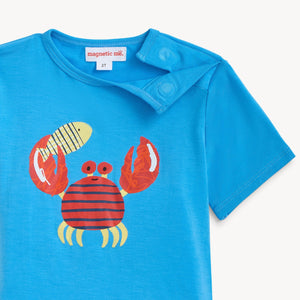 Boys’ Deep Chic Magnetic Top from Magnetic Me features a blue color with a playful red crab and yellow fish graphic on the front, crafted from soft TENCEL™ modal for extra comfort. It includes two snap buttons on the shoulder for easy dressing.