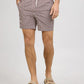 A man stands against a plain light background wearing Onia’s Charles 7″ Swim Trunk, crafted from quick-dry swim fabric with a patterned design and finished with a white drawstring, paired with tan sandals.