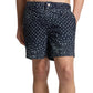 Someone wearing Onia's Calder Buckle 5" Swim Trunk in navy blue with a white paisley print and adjustable waistband, standing with one hand in their pocket.