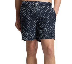 Someone wearing Onia's Calder Buckle 5" Swim Trunk in navy blue with a white paisley print and adjustable waistband, standing with one hand in their pocket.