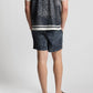 Man stands with his back to the camera, wearing a matching navy blue patterned shirt and Onia Calder Buckle 5" Swim Trunk with adjustable waistband, plus brown sandals, against a plain background.