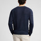 A man faces away from the camera wearing the Onia Silk Linen Crewneck in dark blue with light-colored pants, set against a plain background.