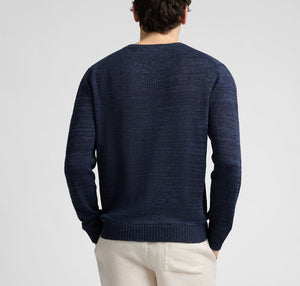 A man faces away from the camera wearing the Onia Silk Linen Crewneck in dark blue with light-colored pants, set against a plain background.