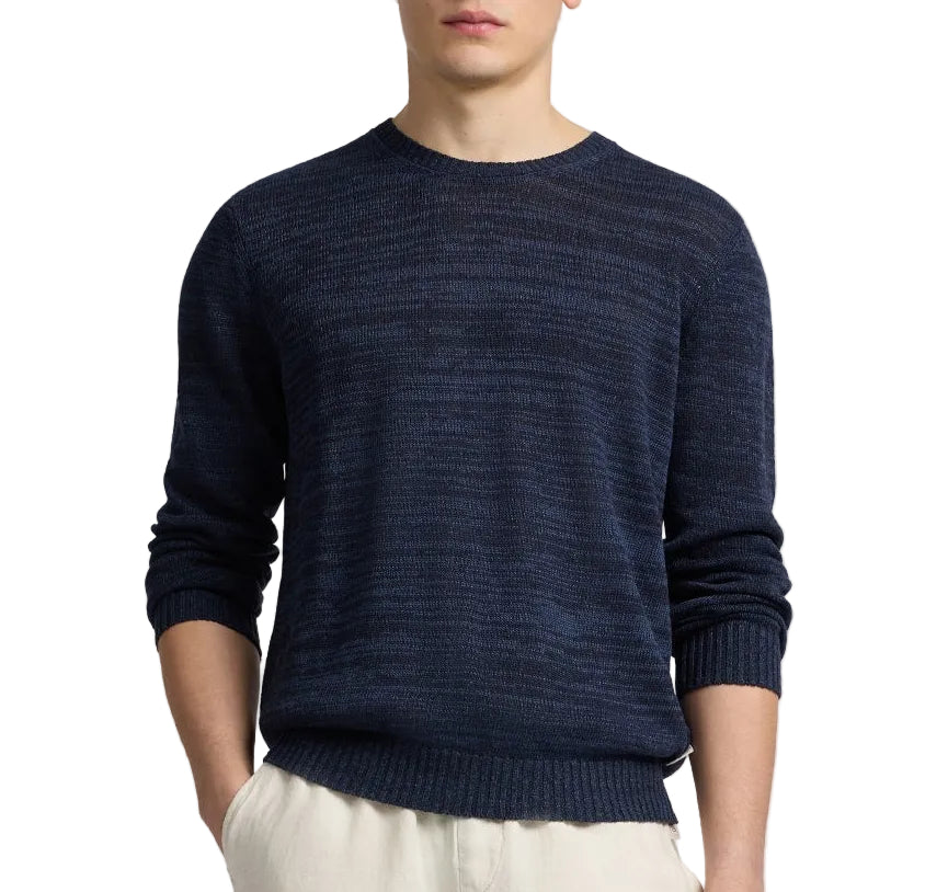 A person wears the Onia Silk Linen Crewneck, a navy blue long-sleeve sweater, with light pants and stands hands-in-pockets against a white background.