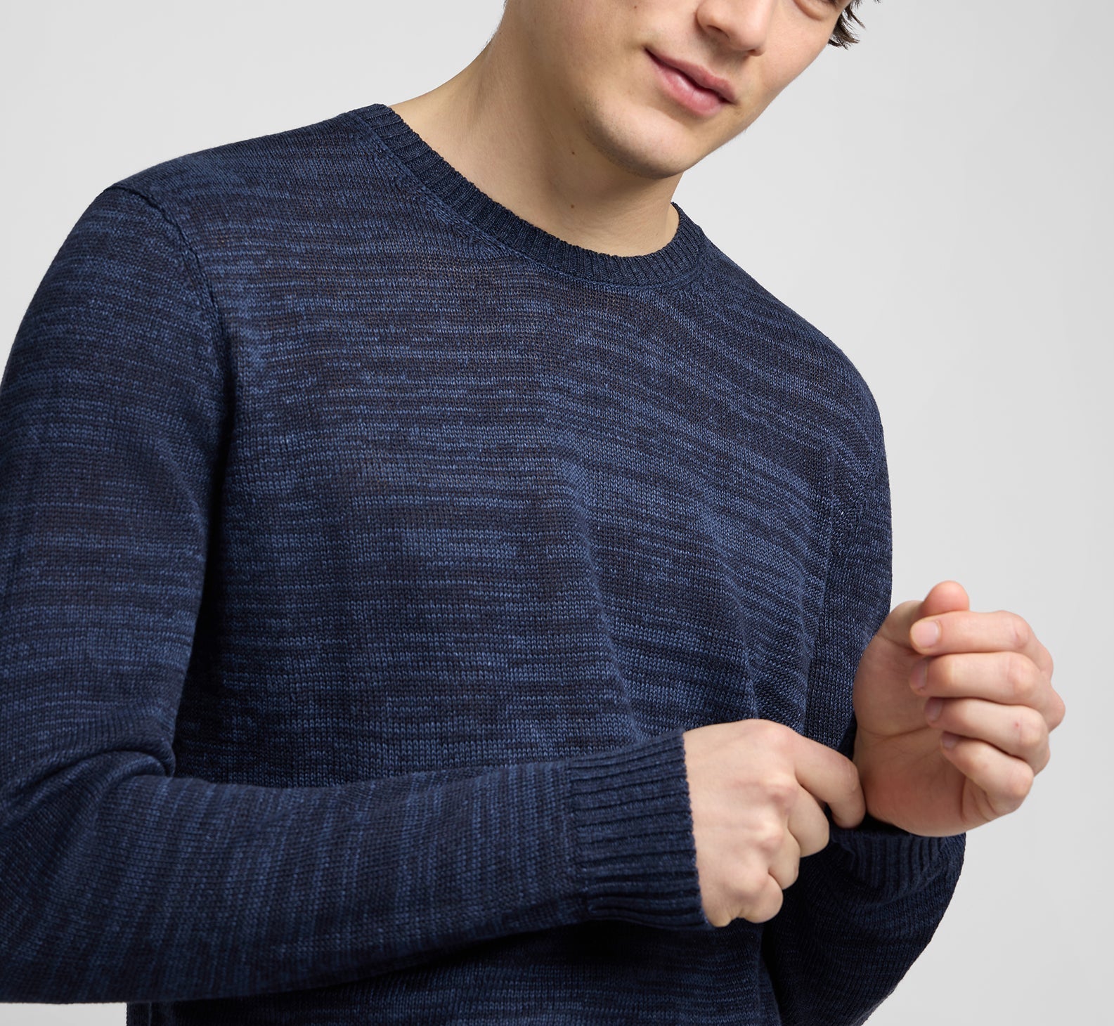 A person adjusts the sleeve of an Onia Silk Linen Crewneck in dark blue, cropped at the mouth and above the waist, against a plain light background—a perfect everyday knit.
