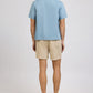 A man faces away, wearing the Onia Air Linen Convertible Vacation Shirt in light blue with short sleeves, paired with beige shorts and brown loafers against a plain light background.