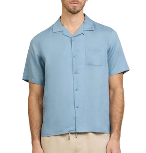 A man wearing the Onia Air Linen Convertible Vacation Shirt in light blue with short sleeves and a chest pocket, paired with beige pants, stands against a white background.