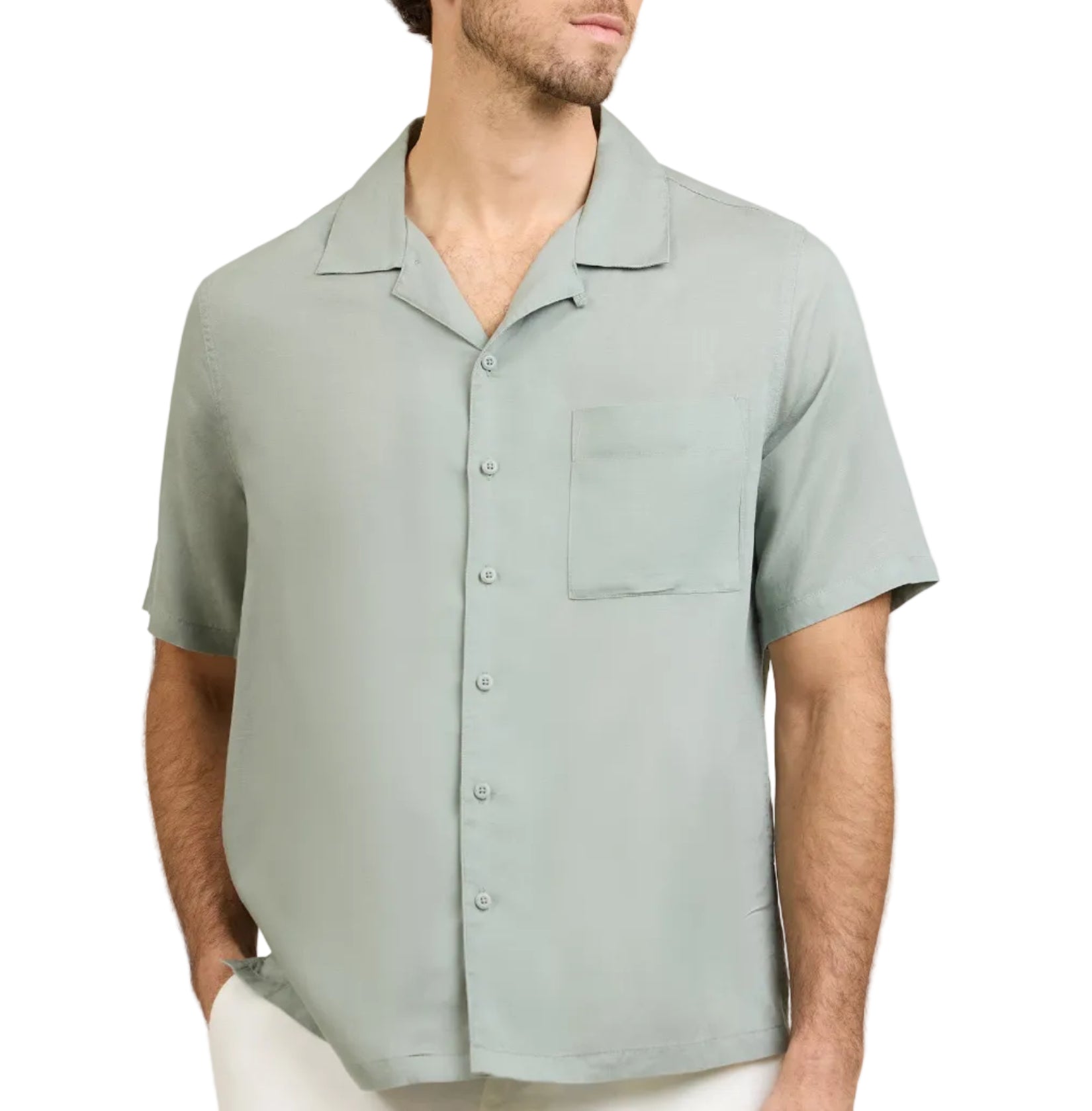 A man wearing the Onia Air Linen Convertible Vacation Shirt in light green with short sleeves and a left chest pocket, paired with white pants, stands with his hands in his pockets.
