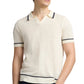 A man wearing the Onia Linen Johnny Collar Polo Sweater—a short-sleeve cream knit with dark trim—stands with one hand in his pocket.