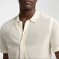 A person wearing the Onia Crochet Knit Button Up—a short-sleeve, cream knit polo shirt with a button front and spread collar, perfect for warm-weather layering.
