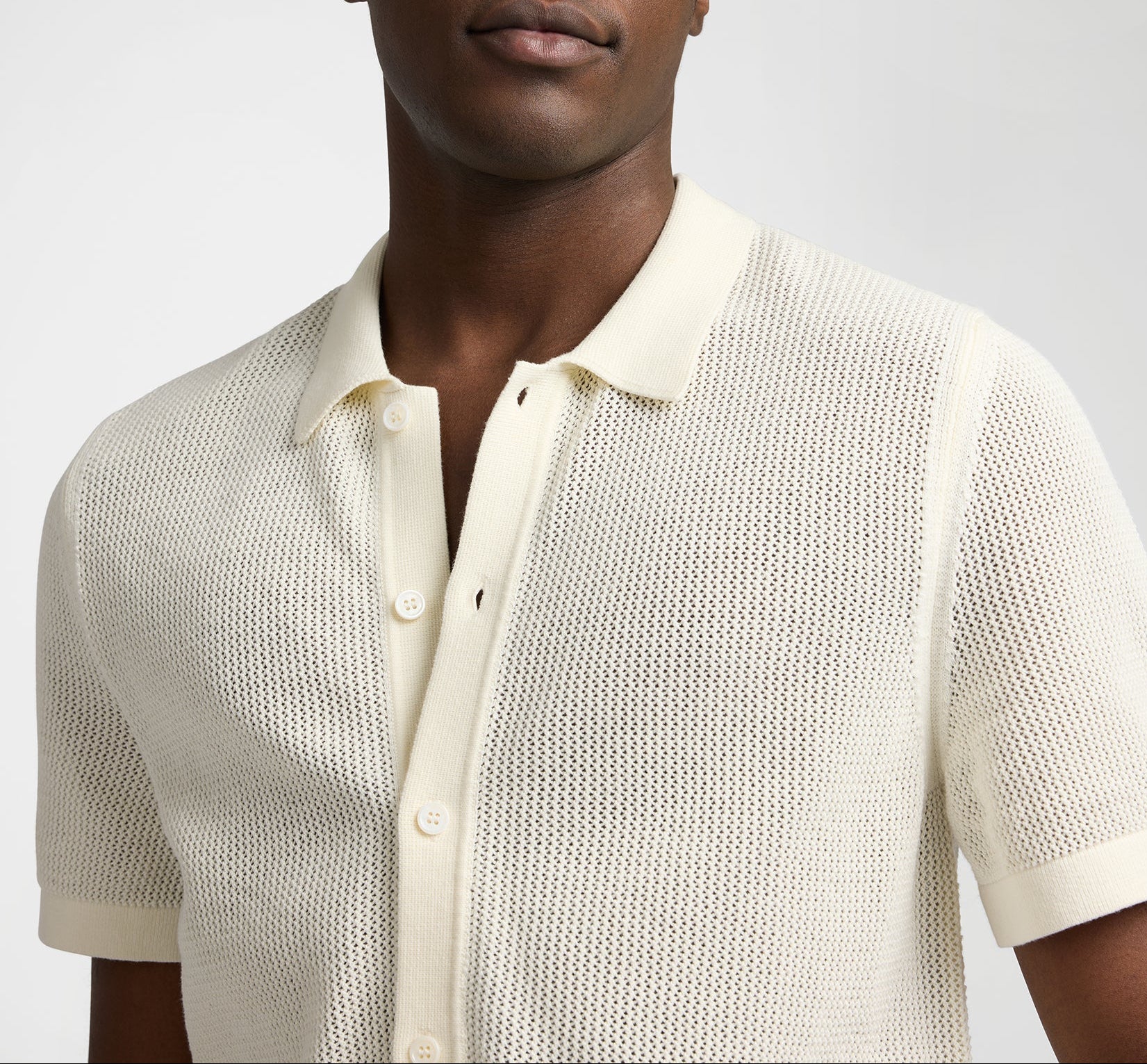 A person wearing the Onia Crochet Knit Button Up—a short-sleeve, cream knit polo shirt with a button front and spread collar, perfect for warm-weather layering.