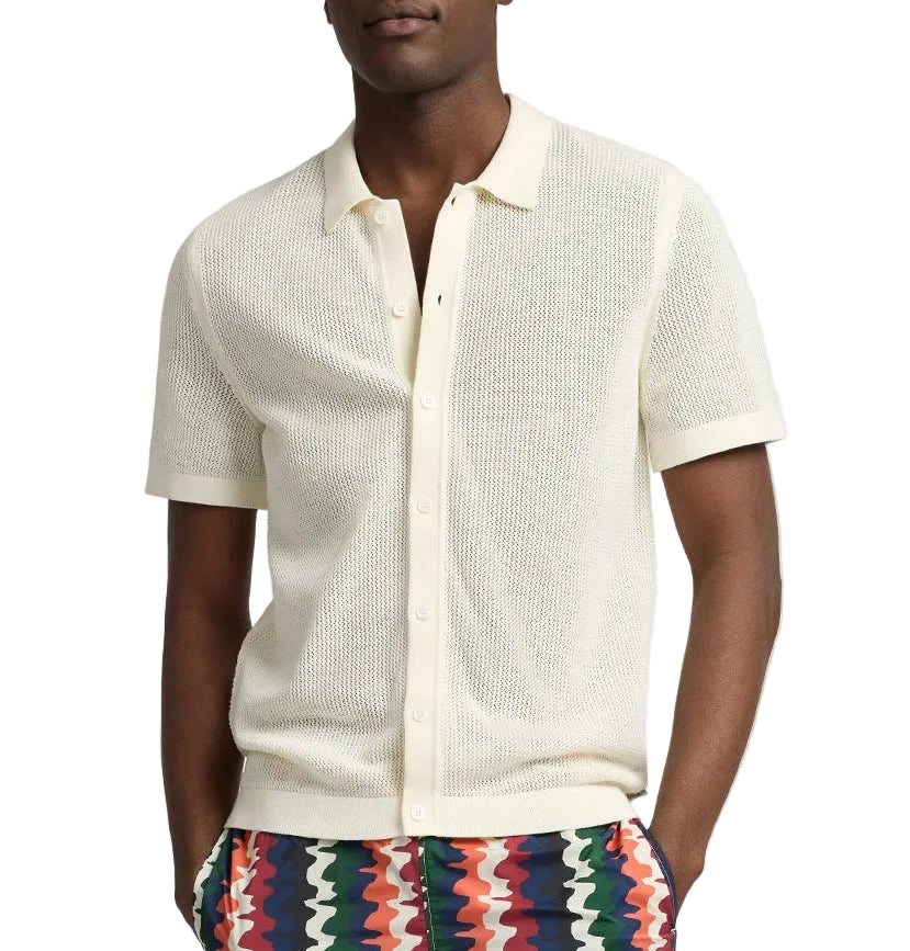 A person wearing the Onia Crochet Knit Button Up, a short-sleeve off-white cotton shirt with a collar, paired with colorful zigzag patterned pants—ideal for warm-weather layering.