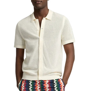 A person wearing the Onia Crochet Knit Button Up, a short-sleeve off-white cotton shirt with a collar, paired with colorful zigzag patterned pants—ideal for warm-weather layering.