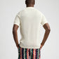 A person faces away, wearing the Onia Crochet Knit Button Up, a short-sleeve white shirt, paired with multicolored zigzag shorts against a plain background.