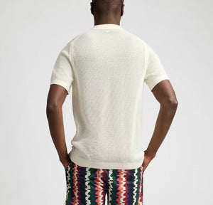 A person faces away, wearing the Onia Crochet Knit Button Up, a short-sleeve white shirt, paired with multicolored zigzag shorts against a plain background.