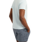 A man stands with his back turned, hands in his pockets, wearing the Onia Joey Crewneck Tee—a relaxed-fit, light-colored short-sleeve shirt—paired with patterned black-and-white shorts.