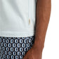 A person wearing the Onia Joey Crewneck Tee in white, visible from the lower half and one arm, paired with geometric blue and white oval-patterned shorts. The tee features a crewneck collar and a small tag.