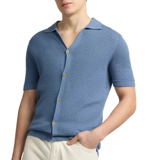 A person wearing the Onia Drop Needle Button Up in light blue, featuring a textured design and collar, paired with cream-colored pants.