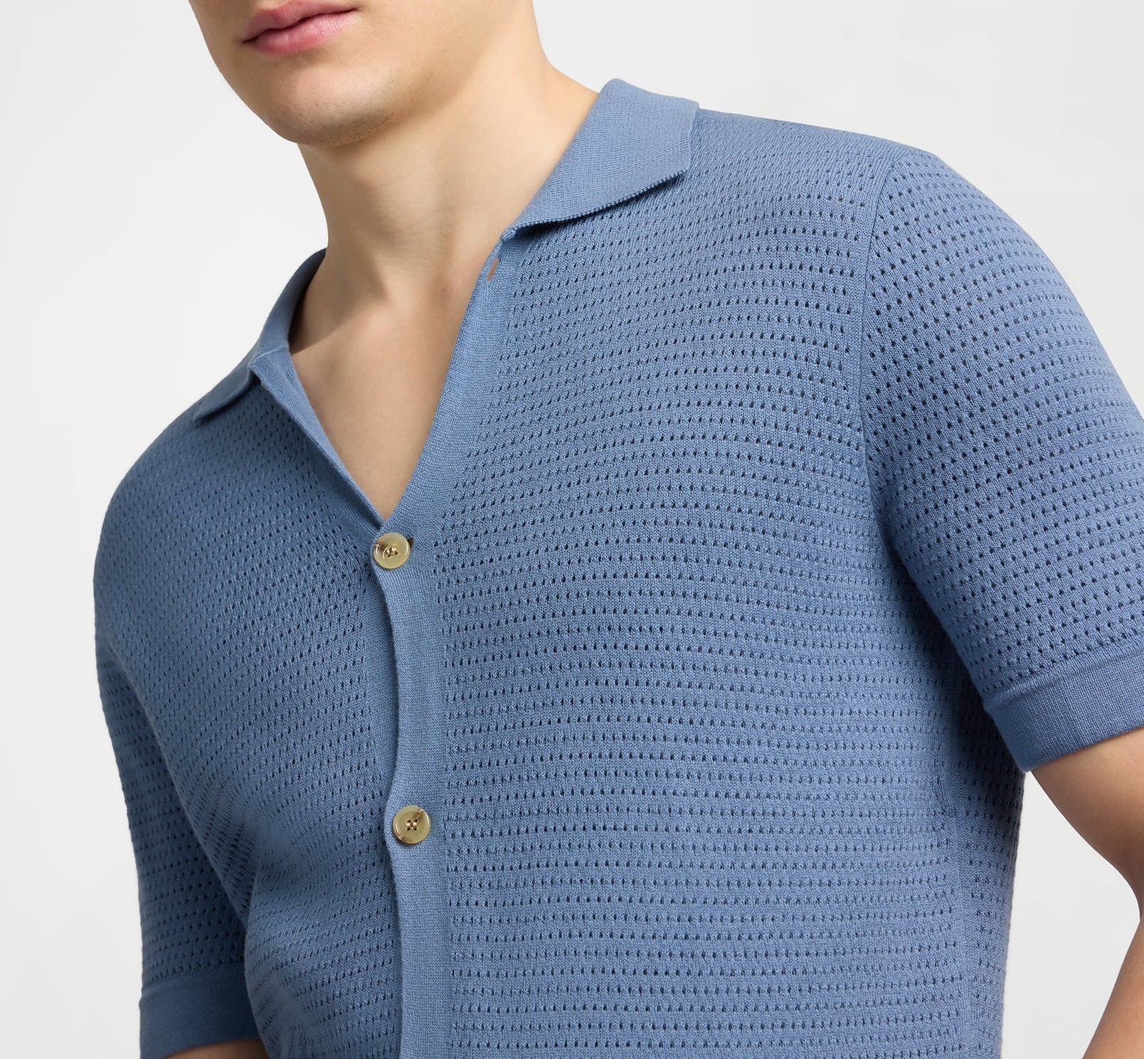 A person wearing the Onia Drop Needle Button Up—a light blue, short-sleeve cotton shirt with textured fabric and two visible buttons—shown from shoulders to mid-torso.
